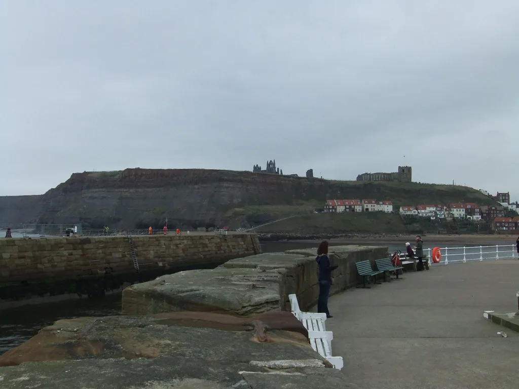The harbour pier in Whitby with the abbey on the clifftop beyond.