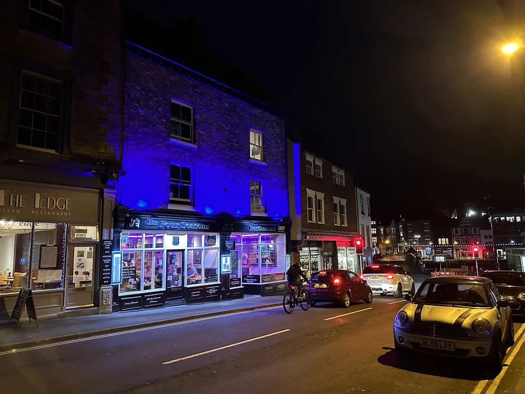 Lit shopfronts on Church Street, Whitby, at night.