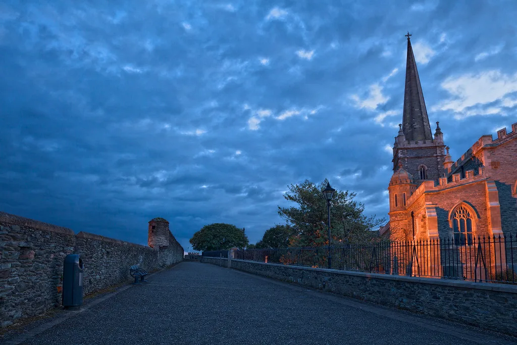 A cathedral spire and the city walls of Derry at twilight.